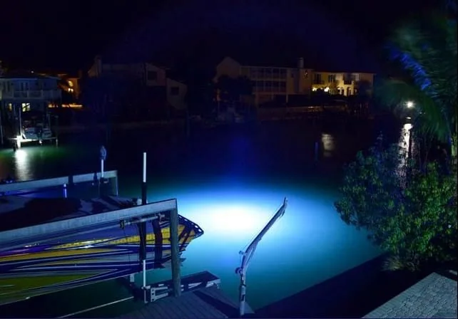 A dock and boat lift at night with light in the water beside it