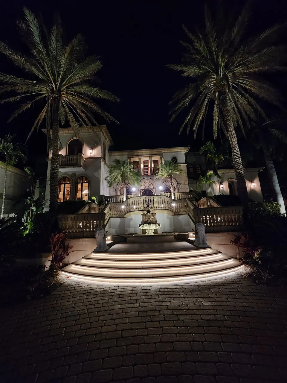 The entry court of a Mediterranean-style house at night with lit arches, balustrades and curved steps