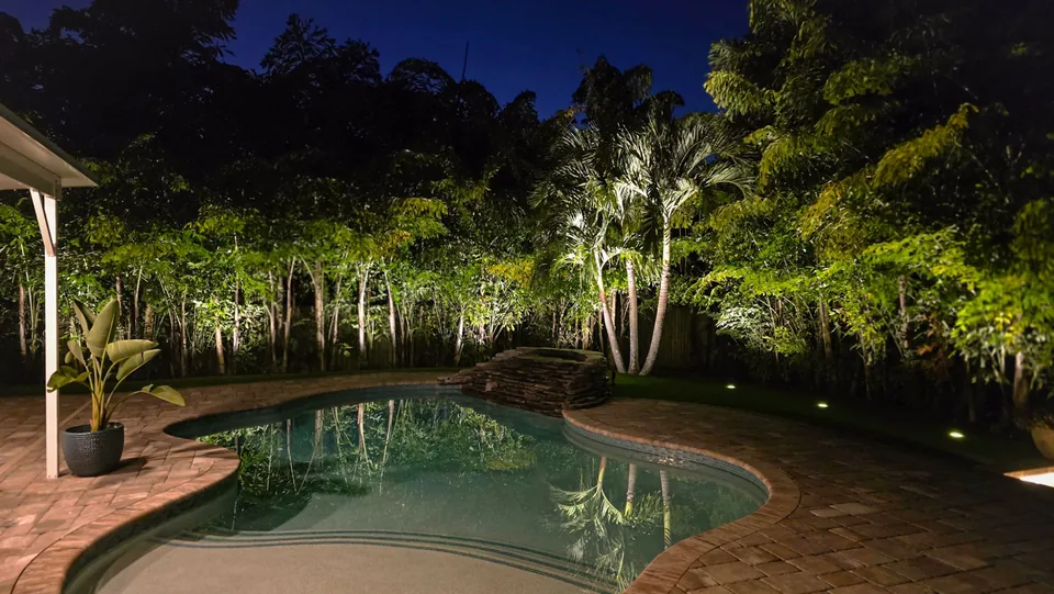 A curved pool reflecting a lit screen of bamboo and palms at dusk