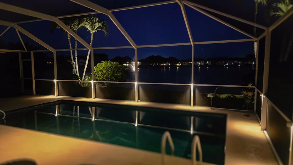 A screened pool enclosure at dusk with a low light at the foot of each post and a lake beyond the screen