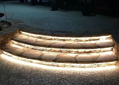 Wide curved stone steps at night with a line of warm light under the front edge of each tread