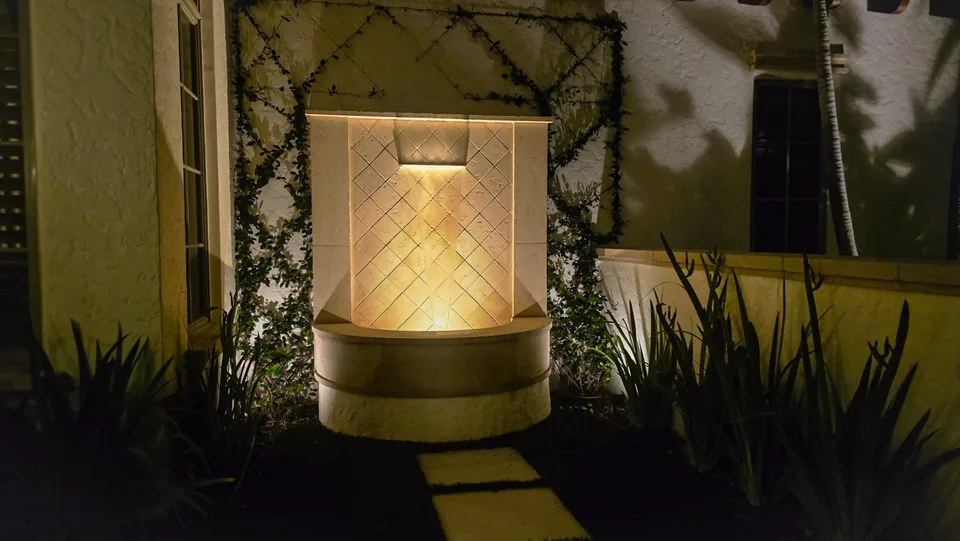 A wall fountain in a stucco courtyard at night, lit warmly from its basin
