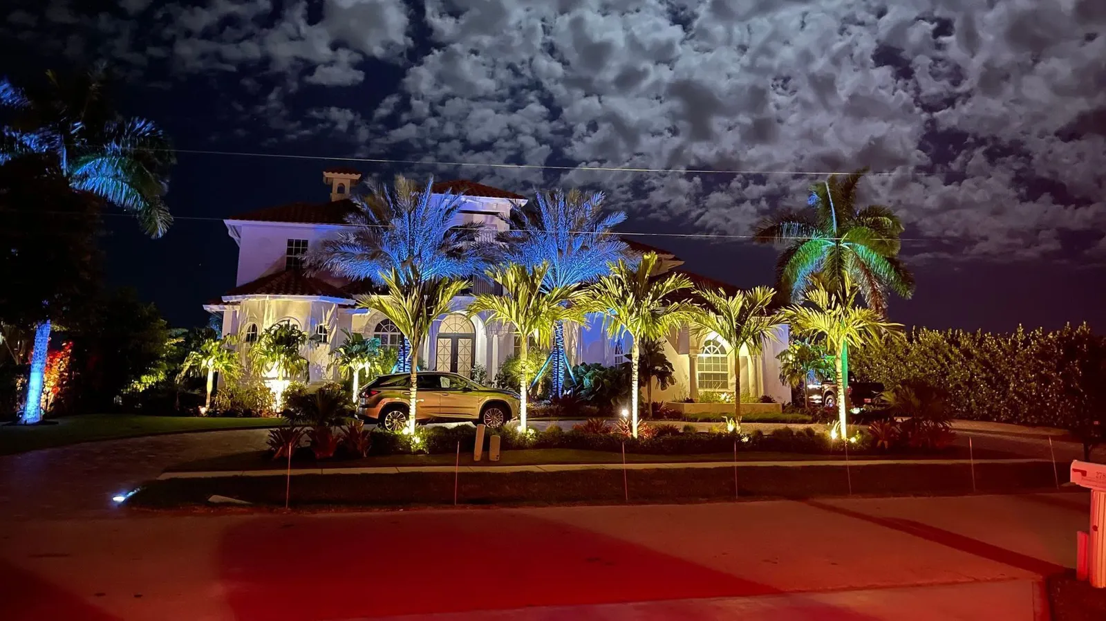 A waterfront home at night with its lighting and color reflected in the water