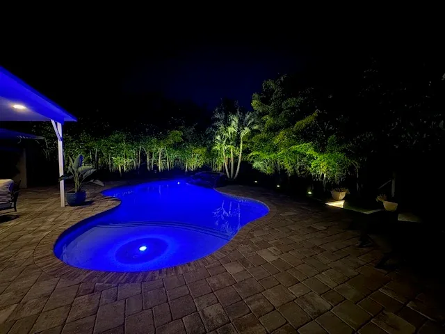 A freeform pool lit blue at night on a coastal property