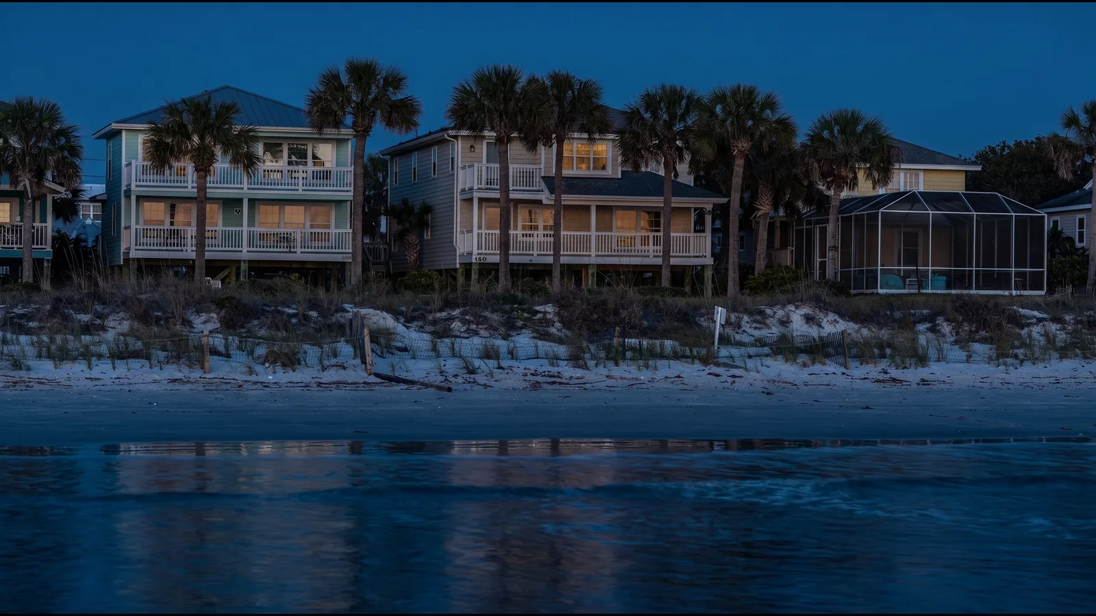 A row of barrier-island beach homes behind a dune, seen from the sand at dusk