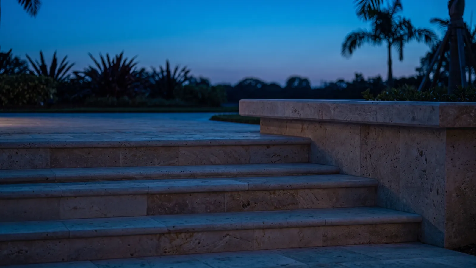 Stone garden steps at dusk, each tread lit by a light under its edge, with uplit planting beyond
