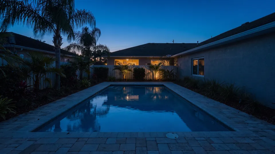 A rectangular pool in a courtyard at dusk, house wall on the right and planting on the left